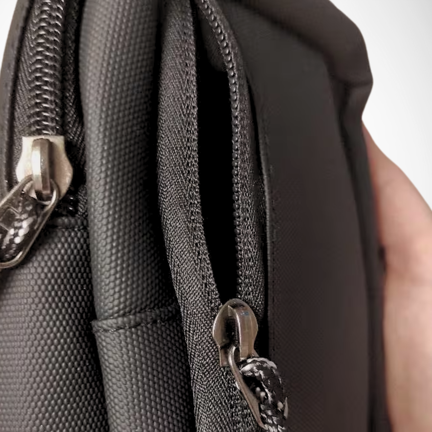 Close-up of a textured black bag with a zipper, held by a person.