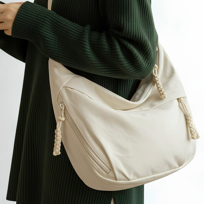 Beige crossbody bag held by a person wearing a green sweater and black skirt.