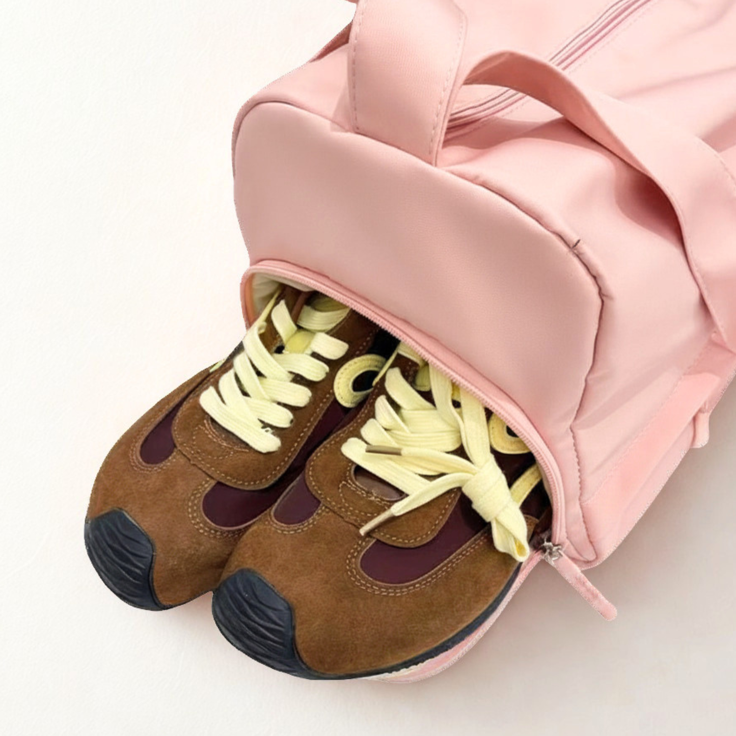 Brown shoes with yellow laces in an open pink duffel bag with a shoe compartment on a white background